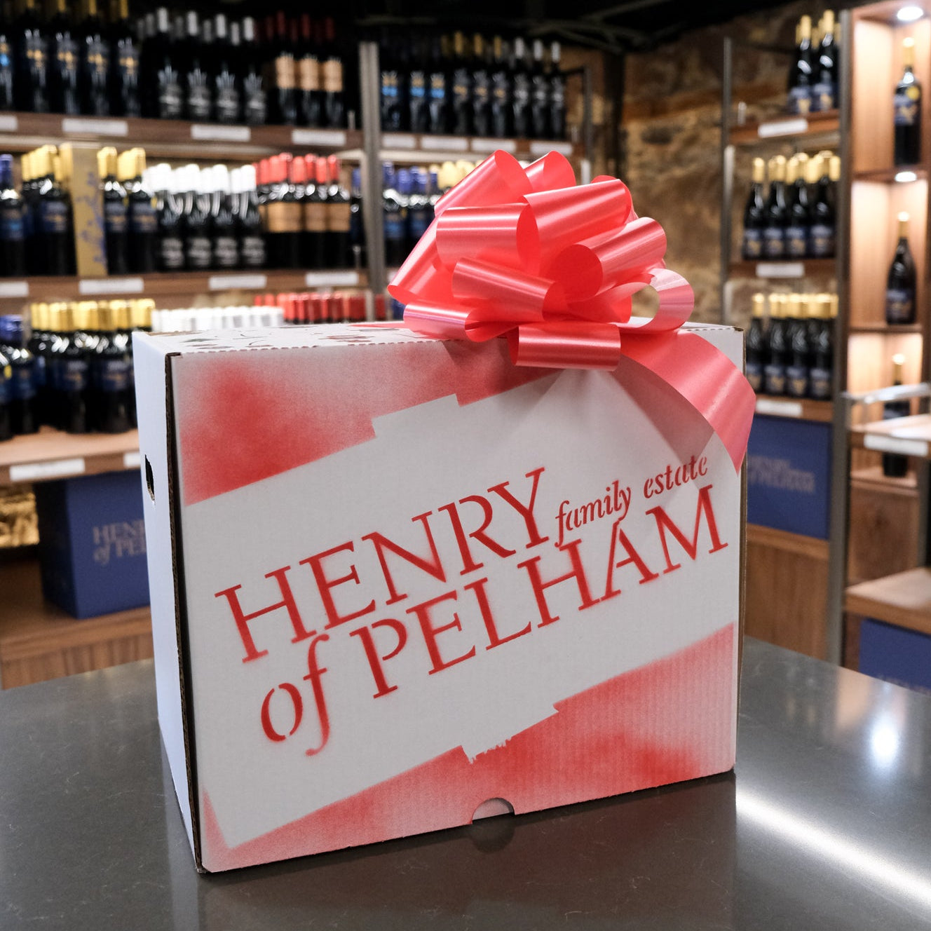 Gift box with a red bow labeled 'Henry of Pelham' in a store setting.